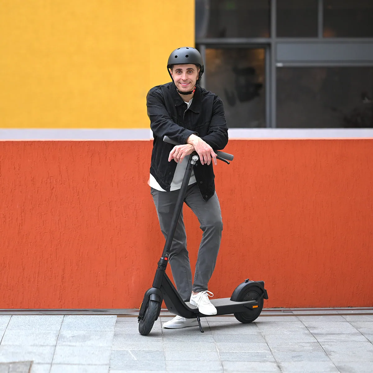 Homme casqué appuyé sur le guidon de l'Inmotion Air devant un mur orange