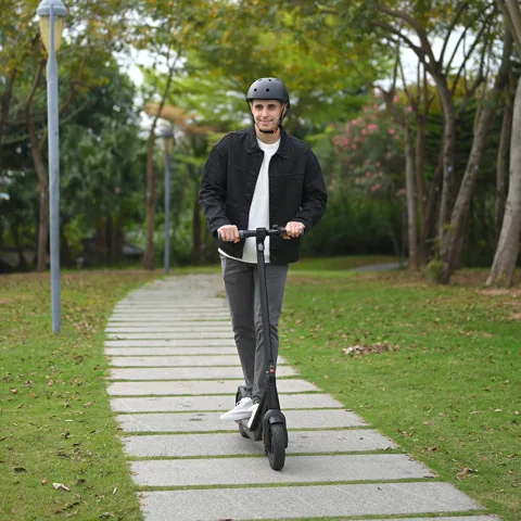 Homme casqué roulant vers l'objectif sur l'Inmotion Air, sur un chemin dallé