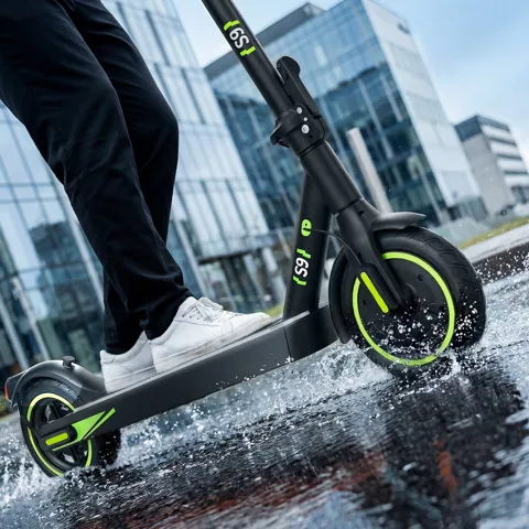 Trottinette électrique isinwheel S9 roulant sur un trottoir mouillé en ville, éclaboussures sous la roue