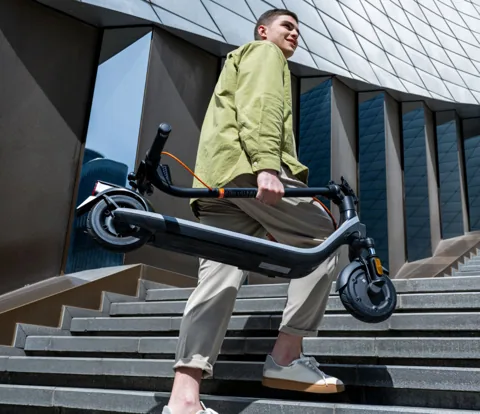 Homme portant une Segway-Ninebot E2 Plus E II pliée en descendant un escalier en ville