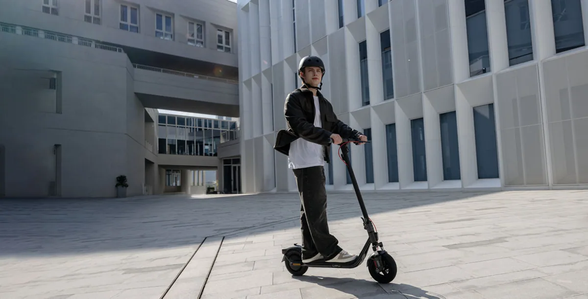 Homme casqué roulant en Segway-Ninebot F2 Pro E II sur une place entre des immeubles blancs