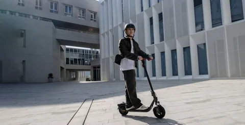 Homme casqué roulant en Segway-Ninebot F2 Pro E II sur une place entre des immeubles blancs