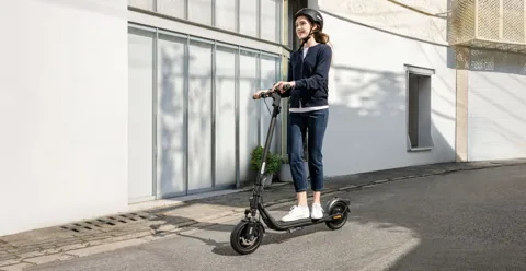 Femme casquée debout sur une Segway-Ninebot F2 E II le long d'un mur blanc