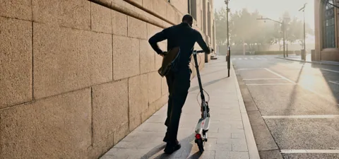 Homme marchant sur un trottoir en tenant une Segway-Ninebot F3 Pro E