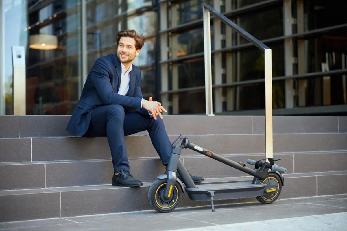 Homme assis sur un muret à côté d'une Segway-Ninebot MAX G30E II pliée