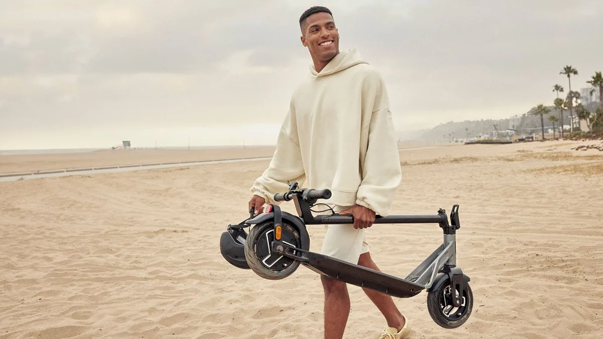 Homme portant une Niu KQi Air pliée sur une plage