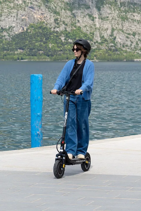 Une femme casquée roule face à l'objectif avec l'Urbanglide Ride 100 Evo sur un quai au bord d'un lac