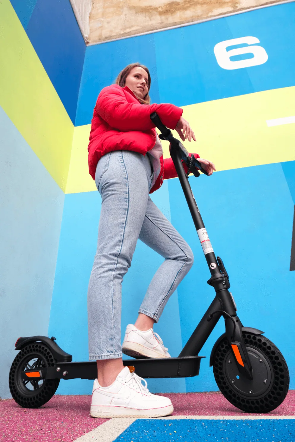 Une jeune femme pose un pied sur le plateau de l'Urbanglide Ride 100XS, dans un décor bleu et jaune
