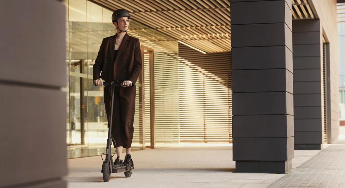 Femme casquée roulant sur la Mi Electric Scooter 1S sous des arcades