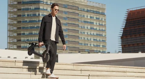 Homme portant sa Mi Electric Scooter 1S pliée en descendant des marches