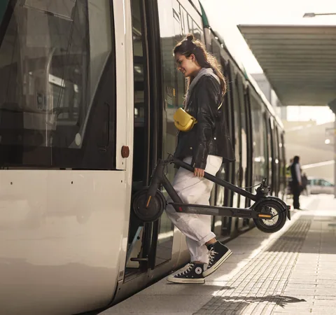 Femme portant sa Mi Electric Scooter Essential pliée en descendant d'un tramway
