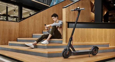 Mi Electric Scooter (M365) noire sur sa béquille près d'un homme assis sur des marches