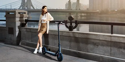 Femme debout à côté de sa Mi Electric Scooter (M365) au bord d'un quai