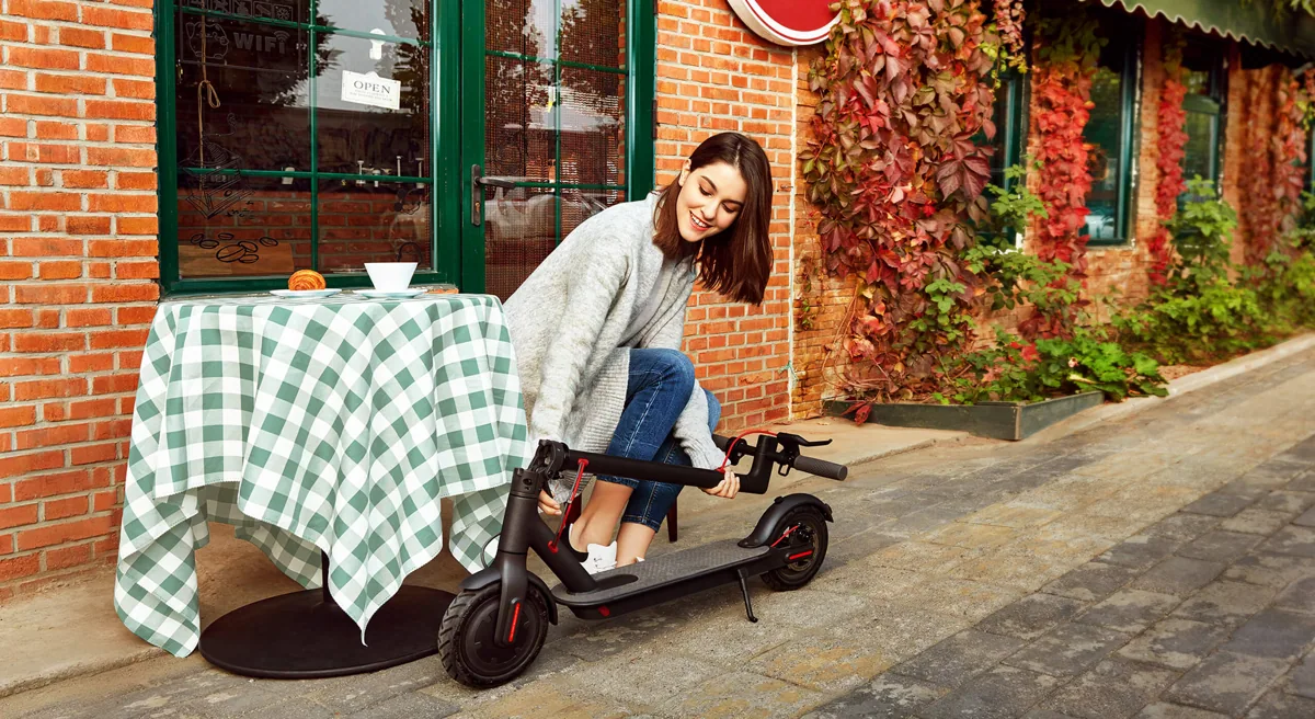 Femme pliant sa Mi Electric Scooter (M365) devant une terrasse de café