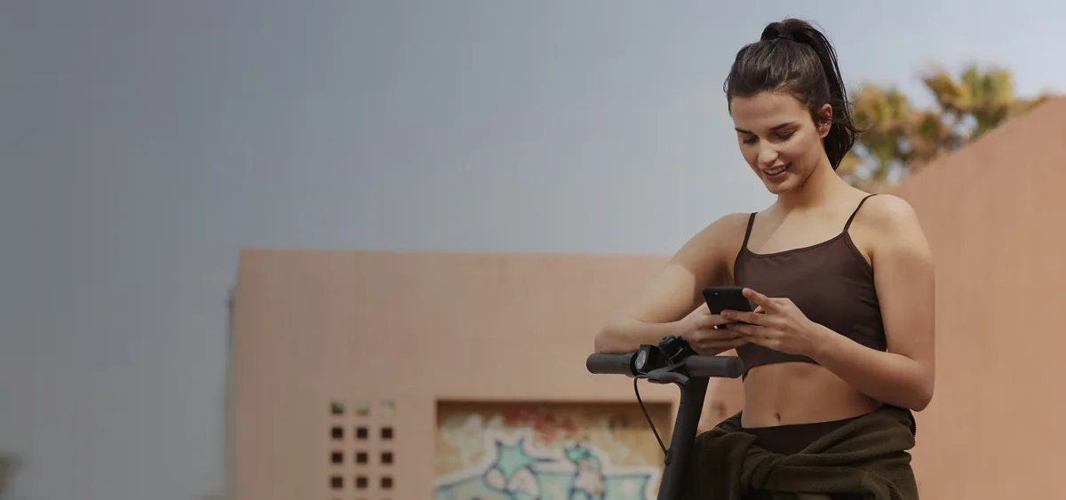 Femme consultant son téléphone à côté du guidon de la Mi Electric Scooter Pro 2