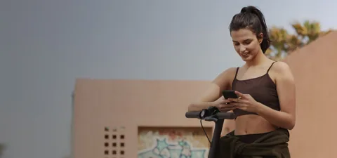 Femme consultant son téléphone à côté du guidon de la Mi Electric Scooter Pro 2