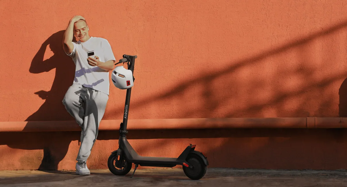 Personne appuyée contre un mur orange à côté de la Xiaomi Electric Scooter 4 Lite (2e génération)