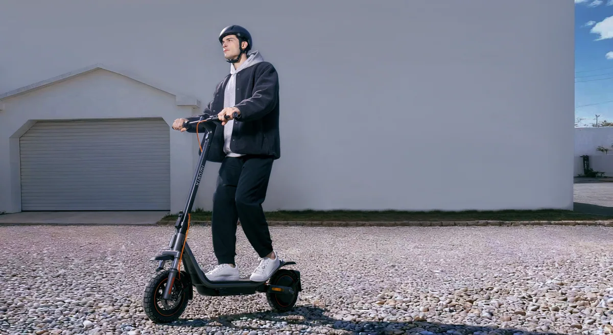 Personne casquée qui roule sur la Xiaomi Electric Scooter 6 Pro sur des graviers devant un garage