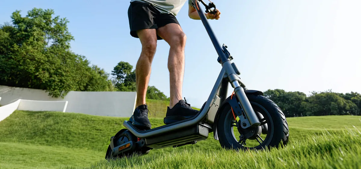Personne qui roule sur la Xiaomi Electric Scooter 6 sur un chemin herbeux, vue basse sur le plateau et la roue arrière