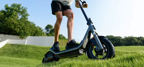 Personne qui roule sur la Xiaomi Electric Scooter 6 sur un chemin herbeux, vue basse sur le plateau et la roue arrière