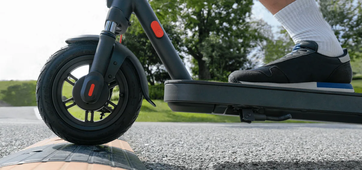Roue avant de la Xiaomi Electric Scooter Elite qui monte sur une bordure, pied de la personne sur le plateau